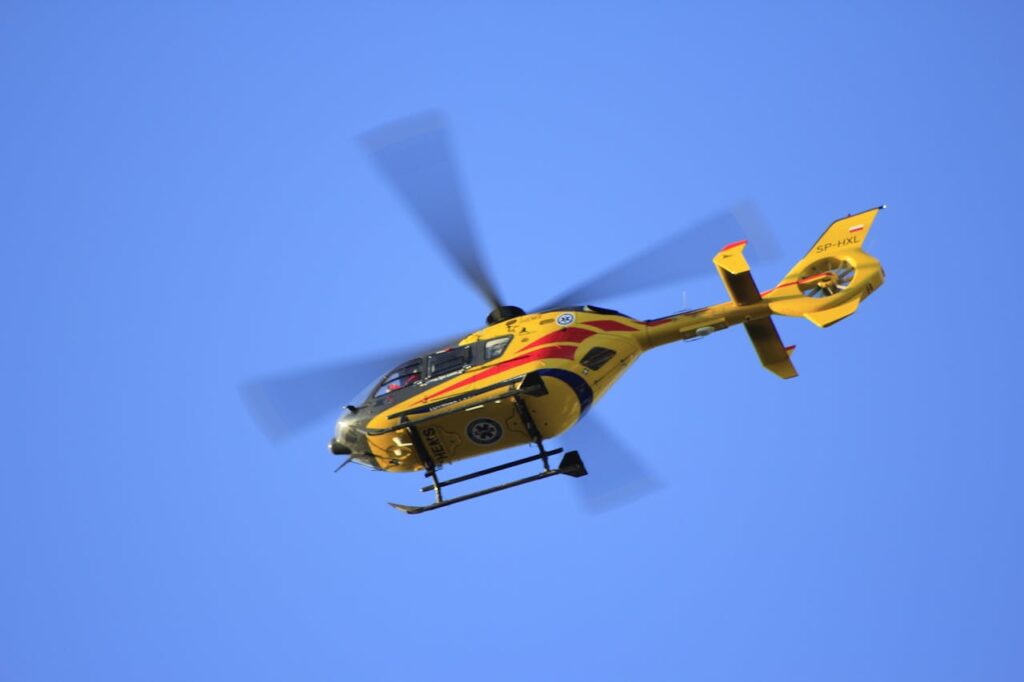 Yellow rescue helicopter in flight against a clear blue sky, showcasing rapid movement.